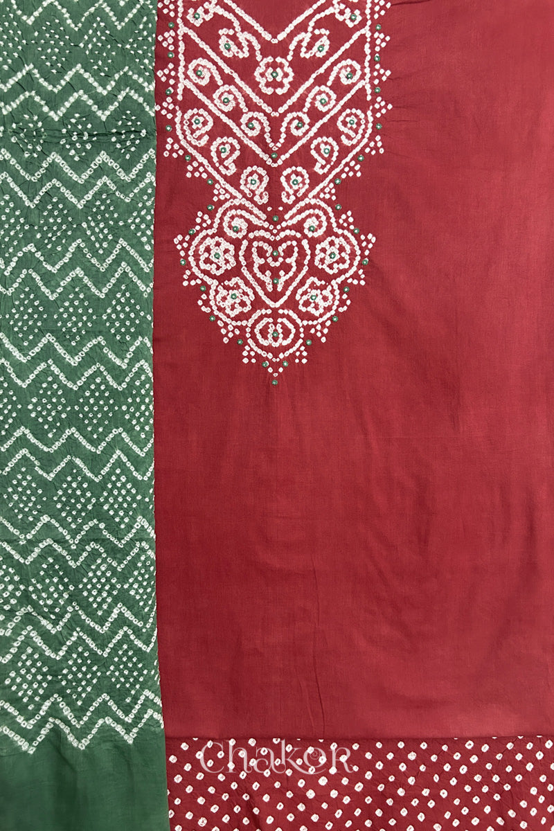 A  brick red kurta set fabric with intricate bandhani & mirror embroidered yoke, paired with a brick red bottom & moss green odhani placed on the left side featuring a zigzag design.