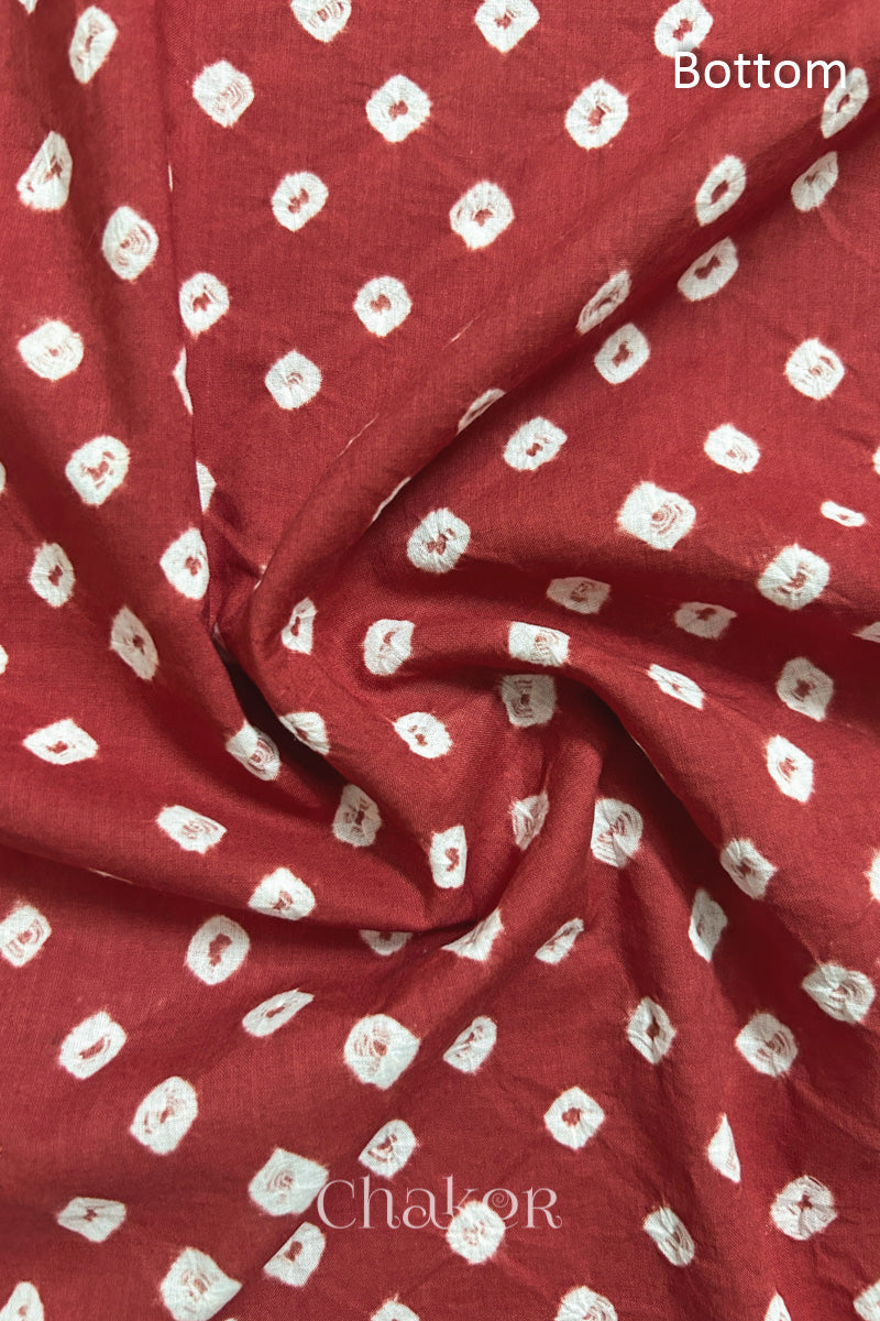 Close-up of brick red fabric featuring bandhani pattern of white dots, showcasing the textile's texture and design details.Text reads bottom details.