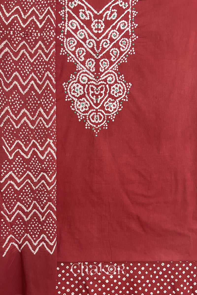 A  brick red kurta set fabric with intricate bandhani & mirror embroidered yoke, paired with a brick red bottom & odhani placed on the left side featuring a zigzag design.
