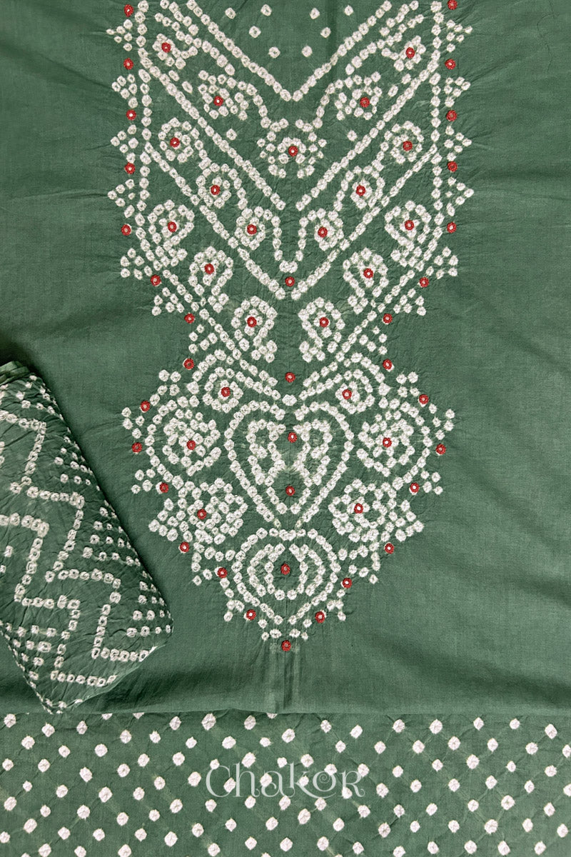 A stylish moss green set fabric featuring mirror embroidered yoke, matching coloured bandhani bottom and dupatta rolled beautifully and placed on the fabric. Text reads Chakor.