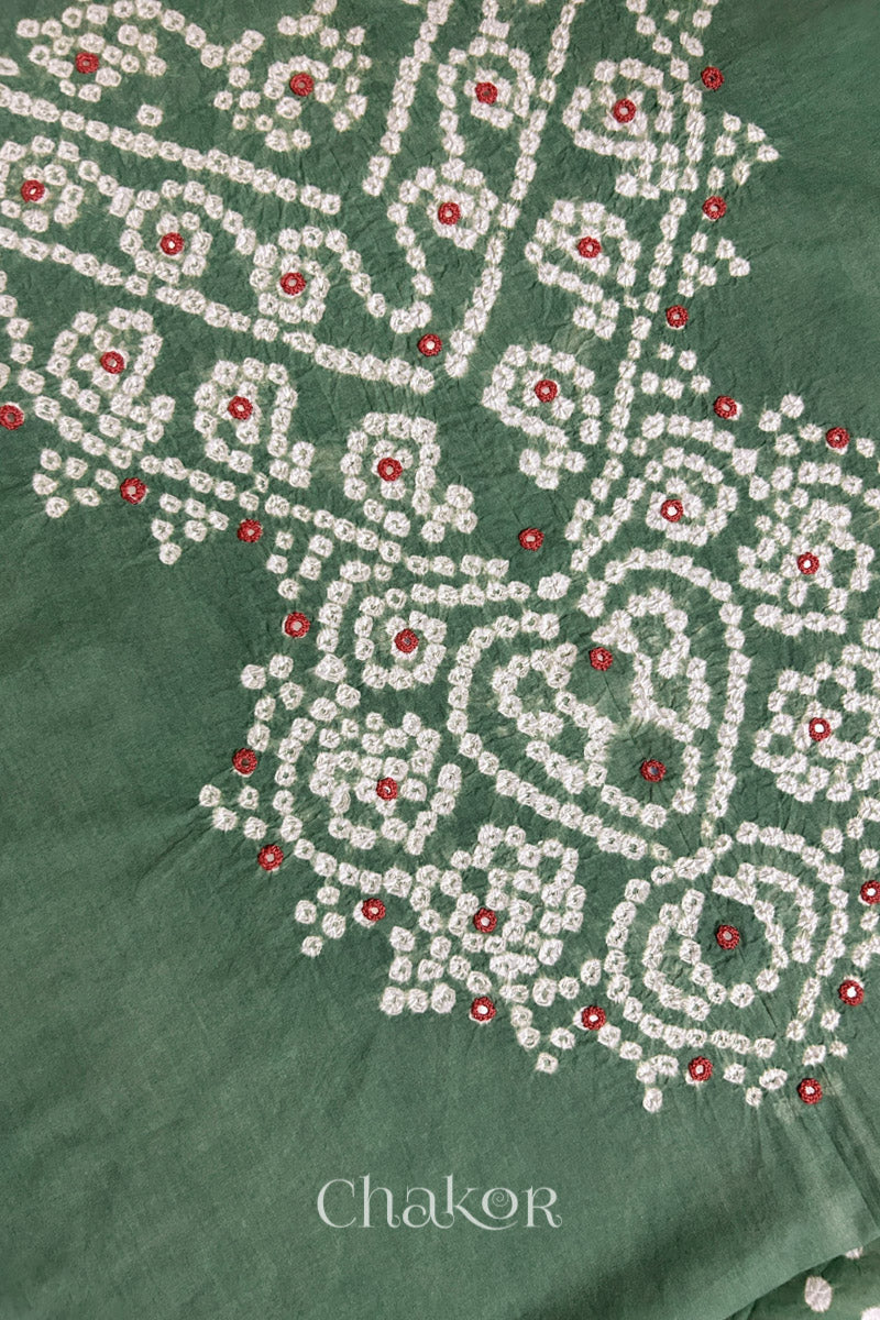 Close-up of  moss green fabric adorned with intricate traditional bandhani patterns and red mirror embroidery, showcasing beautiful craftsmanship.
