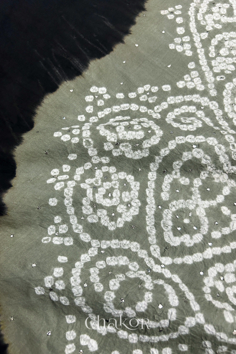 Close-up of  black fabric adorned with intricate traditional bandhani patterns and sparkly mukaish embroidery on cement grey yoke, showcasing beautiful craftsmanship.
