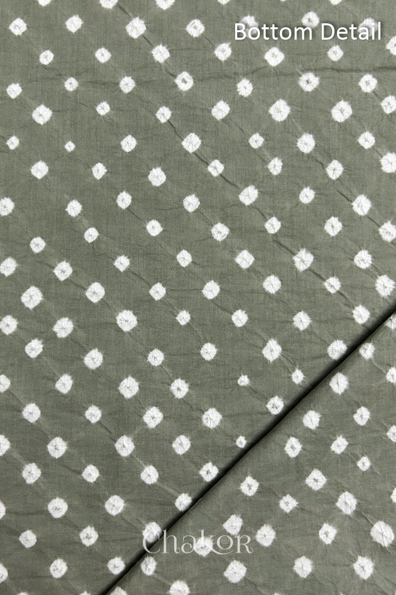 Close up of bottom fabric in cement grey patterned with bandhani tie dye dots, folded at the corner displaying texture and detail. Text reads bottom.
