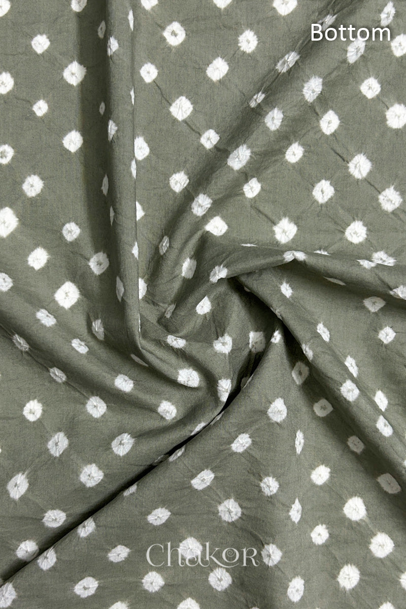 Close-up of cement grey fabric featuring bandhani pattern of white dots, arranged in a swirly style showcasing the textile's texture and design details.Text reads bottom details.

