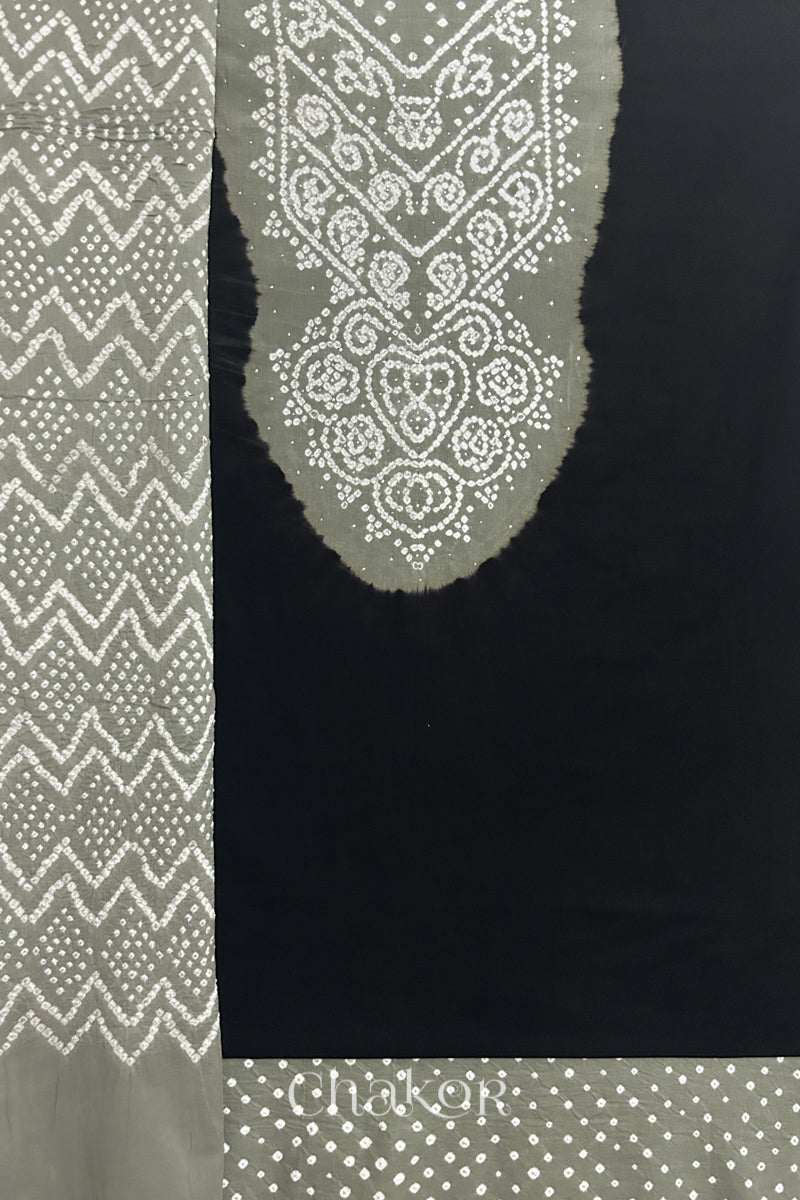 A  black kurta set fabric with intricate bandhani & cement grey yoke with sparkly mukaish embroidery, paired with a bottom & odhani placed on the left side featuring a zigzag design.
