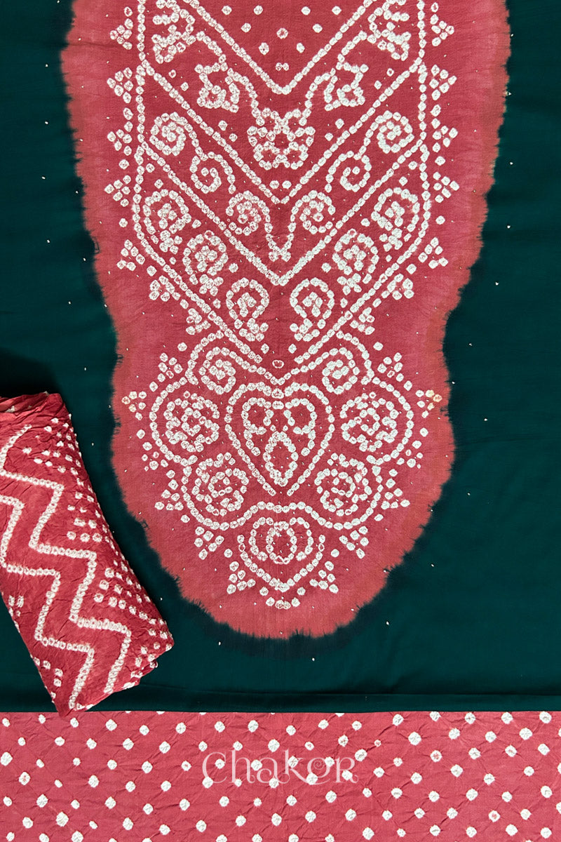 A classic dark green set fabric featuring sparkly mukaish embroidered contrast dusty red yoke & bottom and dupatta rolled beautifully and placed on the fabric. Text reads Chakor.
