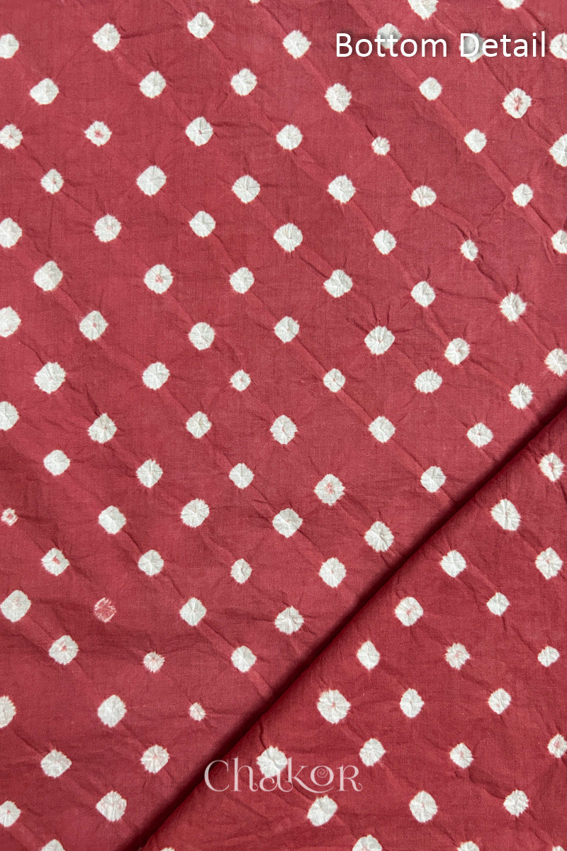 Close up of bottom fabric in dusty red patterned with bandhani tie dye dots, folded at the corner displaying texture and detail. Text reads bottom.
