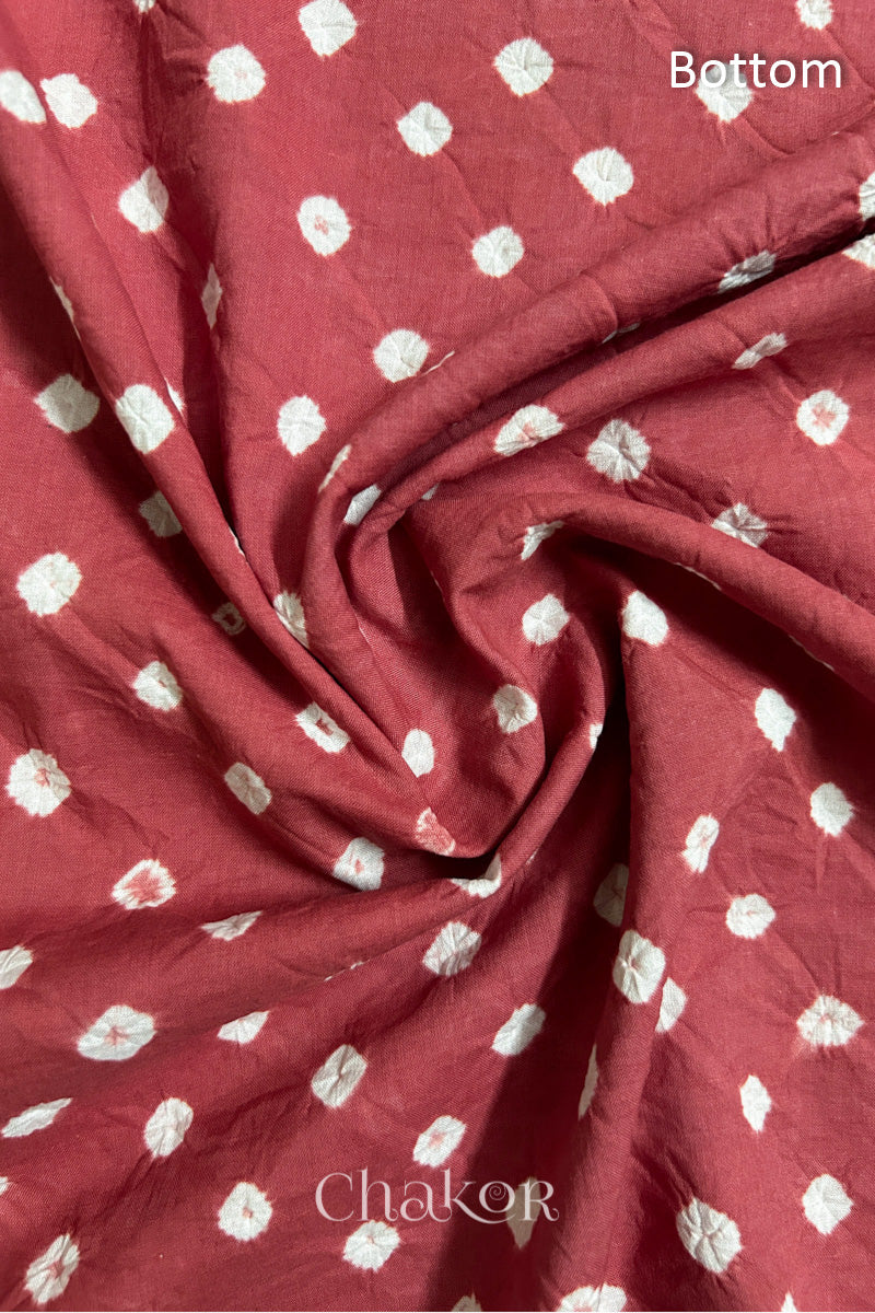 Close-up of dusty red fabric featuring bandhani pattern of white dots, arranged in a swirly style showcasing the textile's texture and design details.Text reads bottom details.