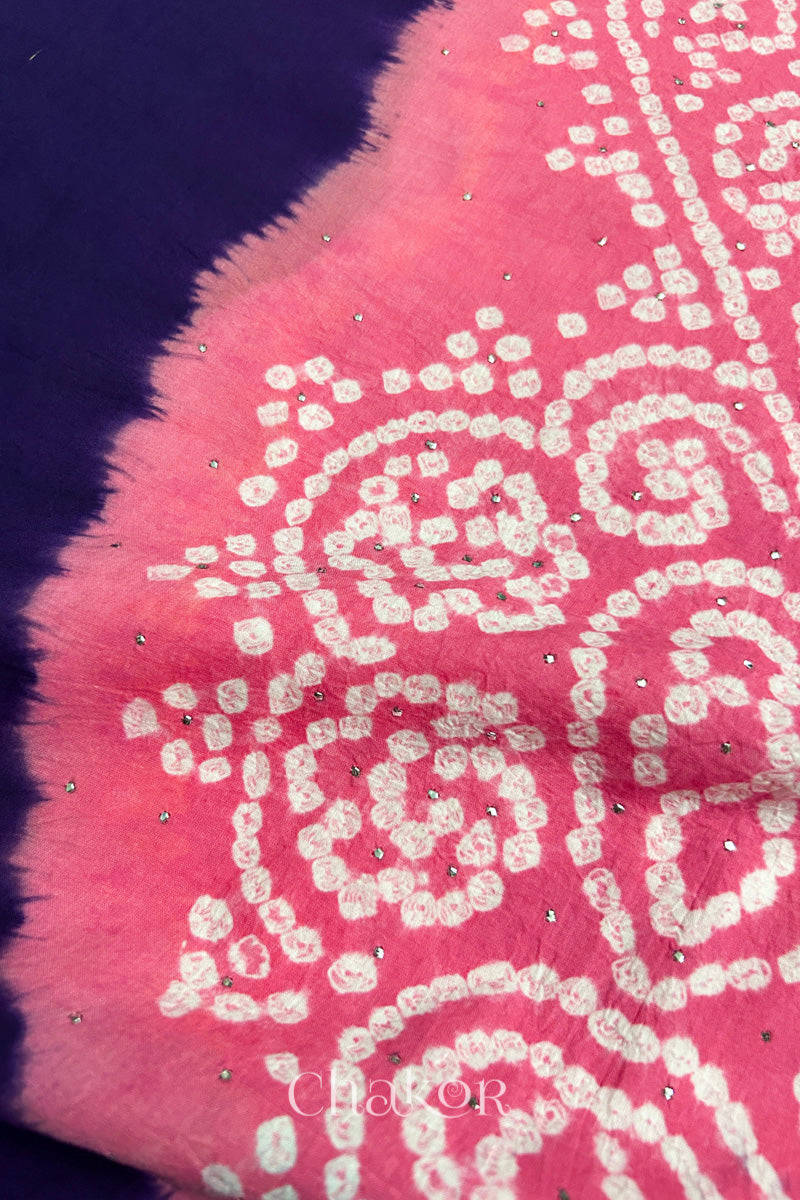 Close-up of dark purple fabric adorned with intricate traditional bandhani patterns and sparkly mukaish embroidery on pink yoke, showcasing beautiful craftsmanship.