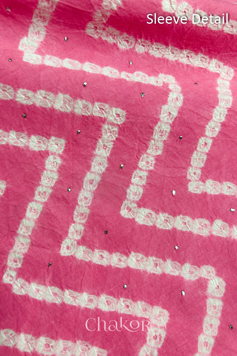 Close-up of pink bandhani fabric featuring chevron tie-dye design, showcasing sparkly mukaish embroidery with Chakor brand watermark. Text reads sleeve details.
