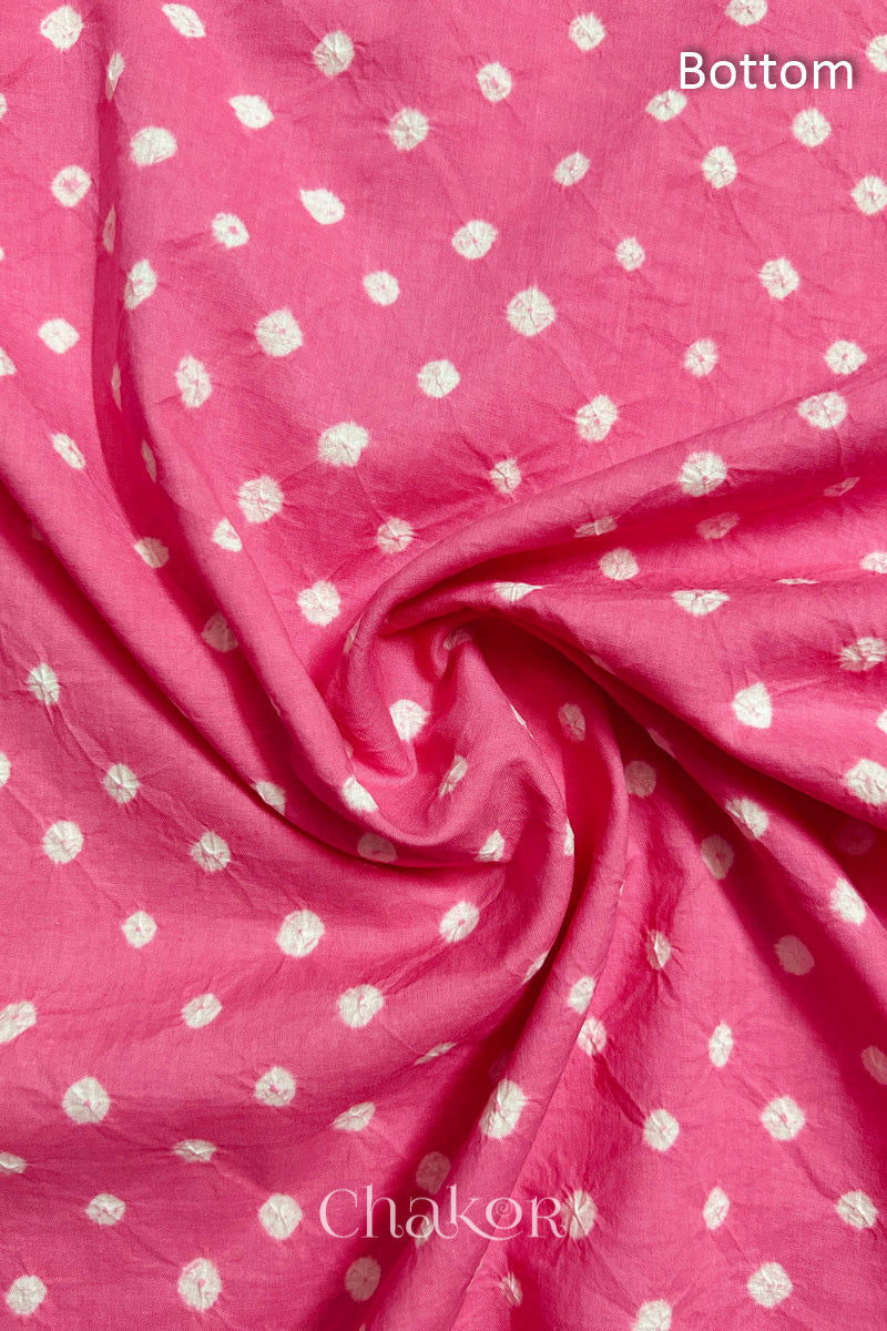 Close-up of pink fabric featuring bandhani pattern of white dots, arranged in a swirly style showcasing the textile's texture and design details.Text reads bottom details.
