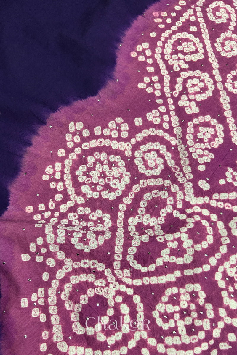 Close-up of dark purple fabric adorned with intricate traditional bandhani patterns and sparkly mukaish embroidery on violet puprle yoke, showcasing beautiful craftsmanship.
