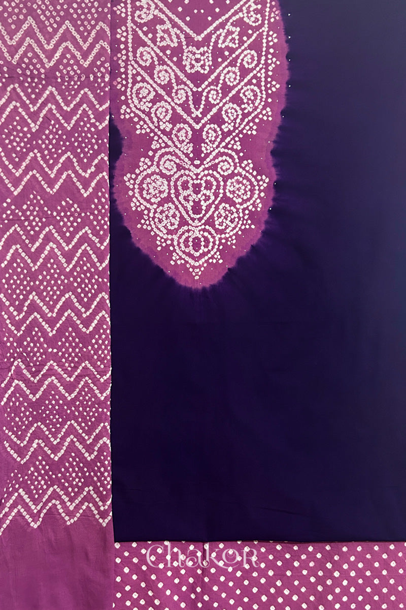 A dark purple kurta set fabric with intricate bandhani & violet puprle yoke with sparkly mukaish embroidery, paired with a bottom & odhani placed on the left side featuring a zigzag design.
