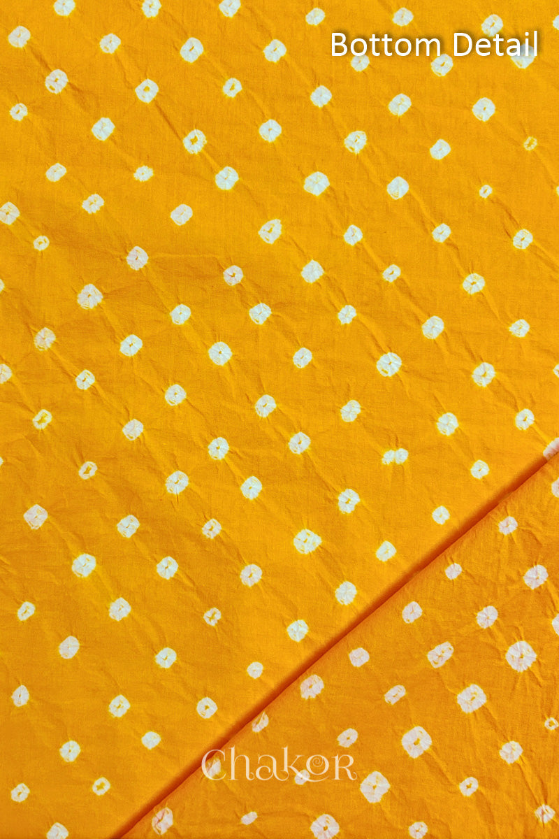 Close up of bottom fabric in yellow patterned with bandhani tie dye dots, folded at the corner displaying texture and detail. Text reads bottom.
