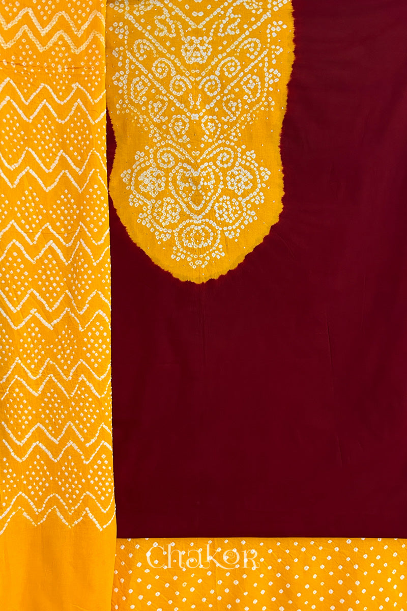 A red kurta set fabric with intricate bandhani & yellow yoke with sparkly mukaish embroidery, paired with a bottom & odhani placed on the left side featuring a zigzag design.
