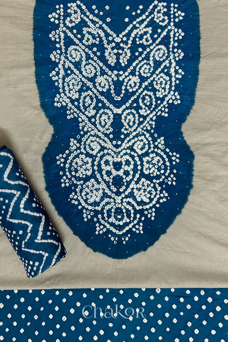 A classic light grey set fabric featuring sparkly mukaish embroidered contrast indigo blue yoke & bottom and dupatta rolled beautifully and placed on the fabric. Text reads Chakor.
