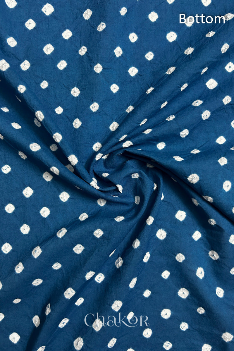 Close-up of indigo blue fabric featuring bandhani pattern of white dots, arranged in a swirly style showcasing the textile's texture and design details.Text reads bottom details.
