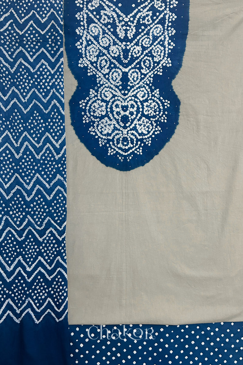 A  light grey kurta set fabric with intricate bandhani & indigo blue yoke with sparkly mukaish embroidery, paired with a bottom & odhani placed on the left side featuring a zigzag design.
