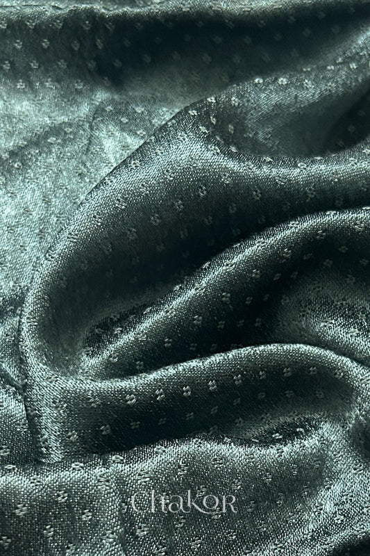 Close-up of charcoal grey mashru self textured fabric with 'Chakor' logo visible.
