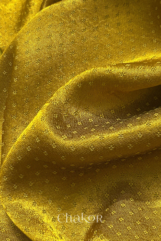 Close-up of mustard yellow mashru self textured fabric with 'Chakor' logo visible.

