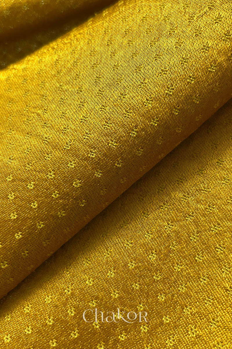 Close-up of mustard yellow mashru self textured fabric with 'Chakor' logo visible.

