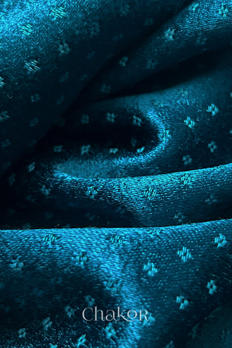Close-up of deep indigo mashru self textured fabric arranged in a swirling design with 'Chakor' logo visible.
