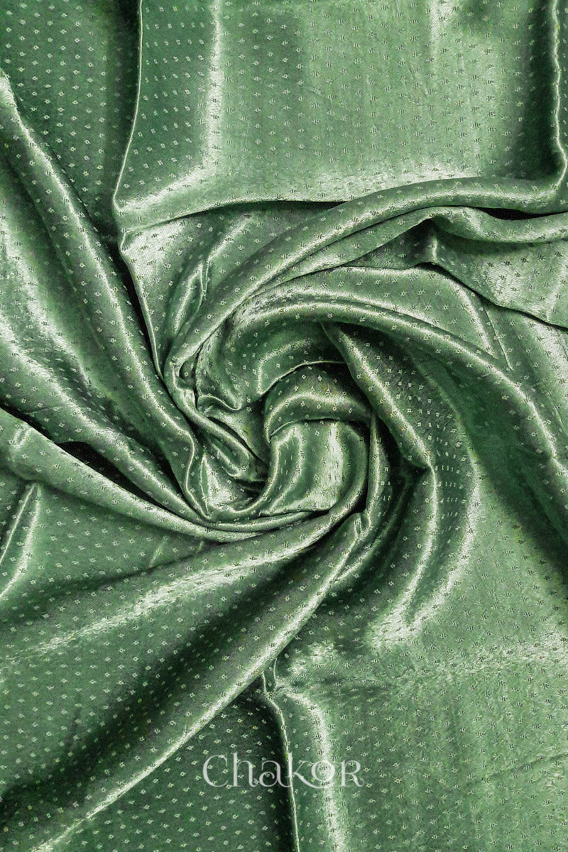 Close-up of pista green mashru self textured fabric arranged in a swirling design with 'Chakor' logo visible.