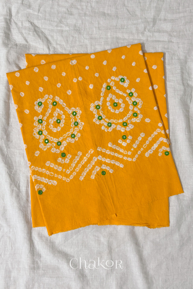 Yellow Kutch Bandhani cotton unstitched blouse fabric with Keri pattern piece folded on white fabric.
