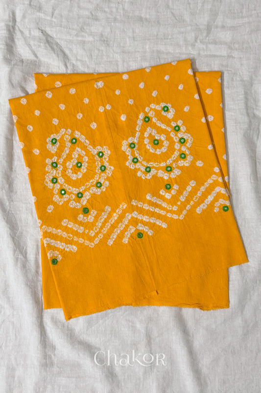 Yellow Kutch Bandhani cotton unstitched blouse fabric with Keri pattern piece folded on white fabric.
