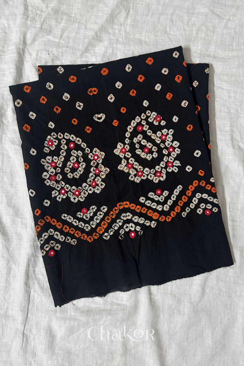 Black Kutch Bandhani cotton unstitched blouse fabric with Keri pattern piece folded on white fabric.

