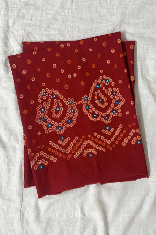 Red Kutch Bandhani cotton unstitched blouse fabric with Keri pattern piece folded on white fabric.
