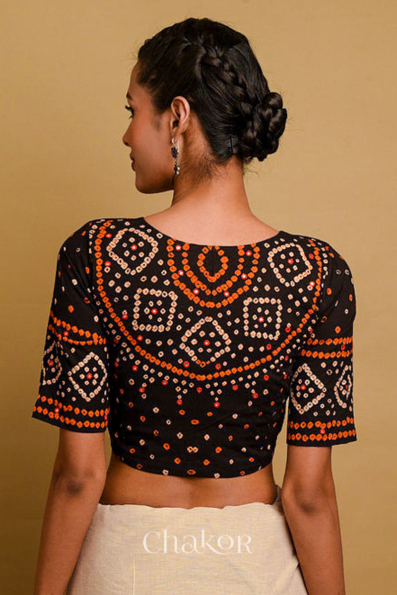 Woman wearing a handcrafted black bandhani cotton blouse in traditional patterns with mirror embroidery.
