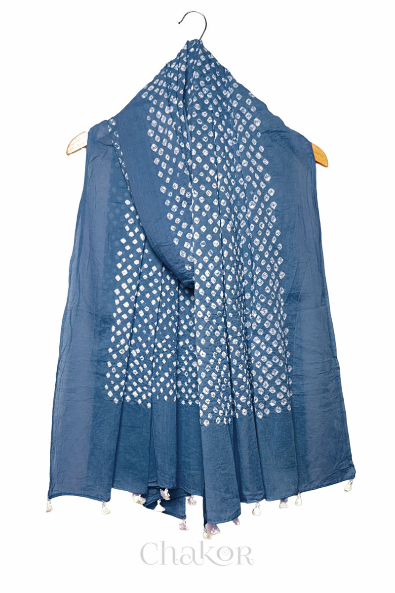 Chakor's blue grey cotton dupatta adorned with white bandhani dots, draped elegantly on a wooden hanger, featuring tassels at the ends.
