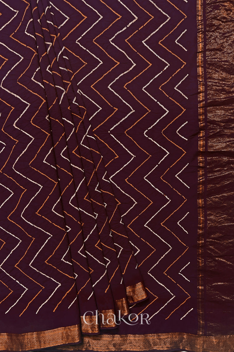 Maroon saree, neatly arranged in pleats with Rai Bandhej zigzag pattern and 'Chakor' brand watermark.

