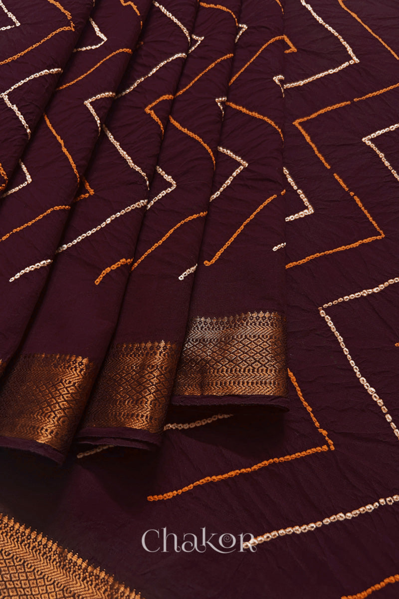 Close-up of Maroon saree pleats with rai bandhani and zari weaving showcasing beautiful craftsmanship.
