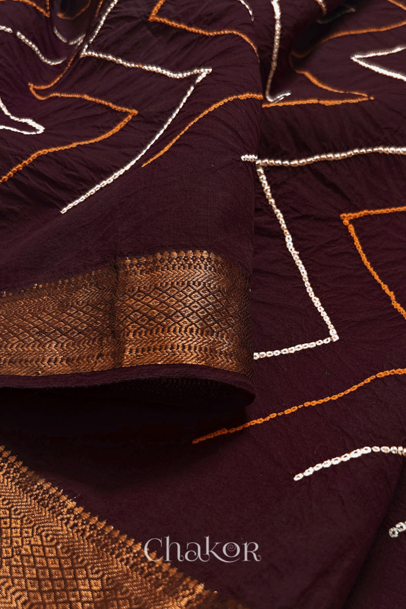 Close-up of Maroon sarees featuring rai bandhani and zari weaving showcasing beautiful craftsmanship.
