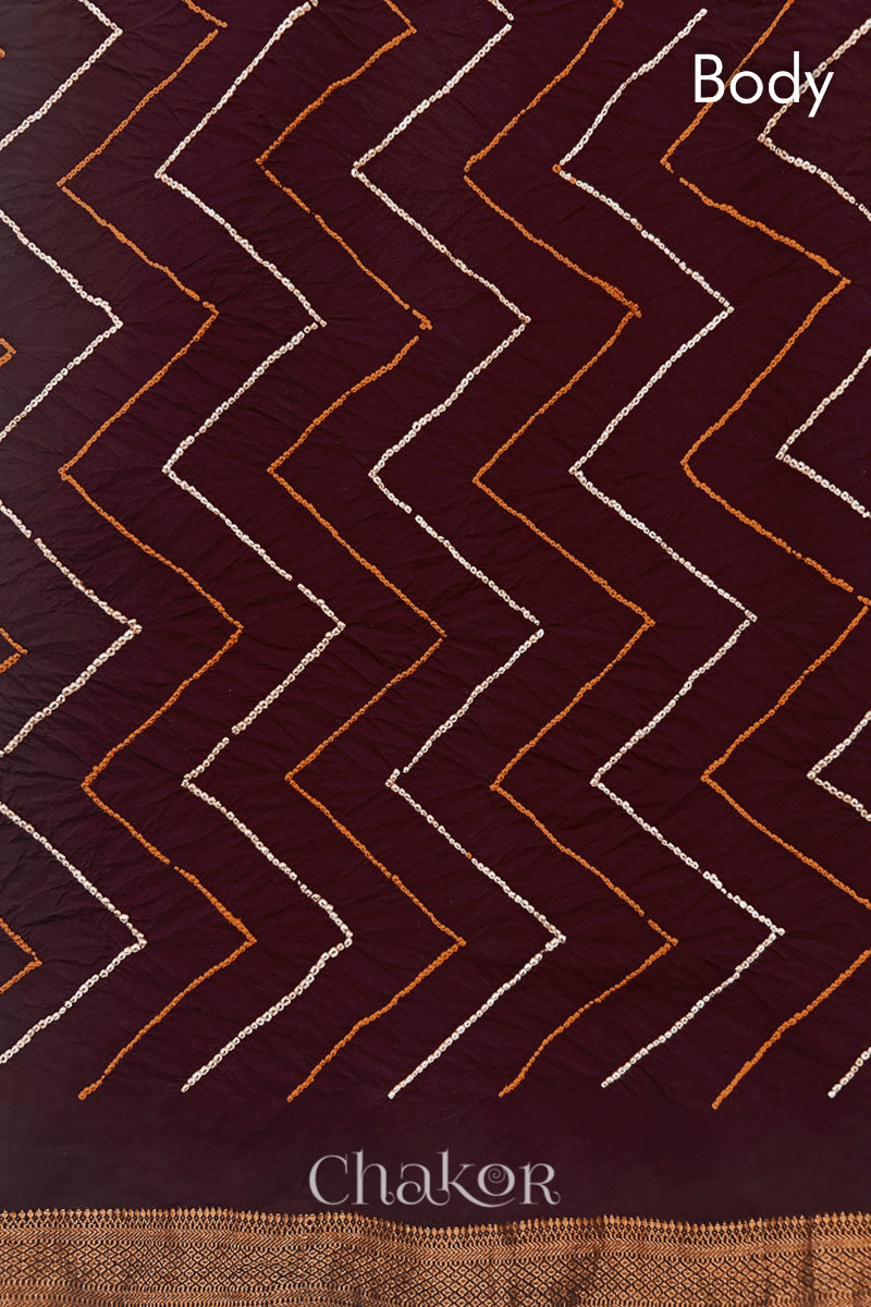 Body detail of Maroon bandhani saree with woven golden zari border.
