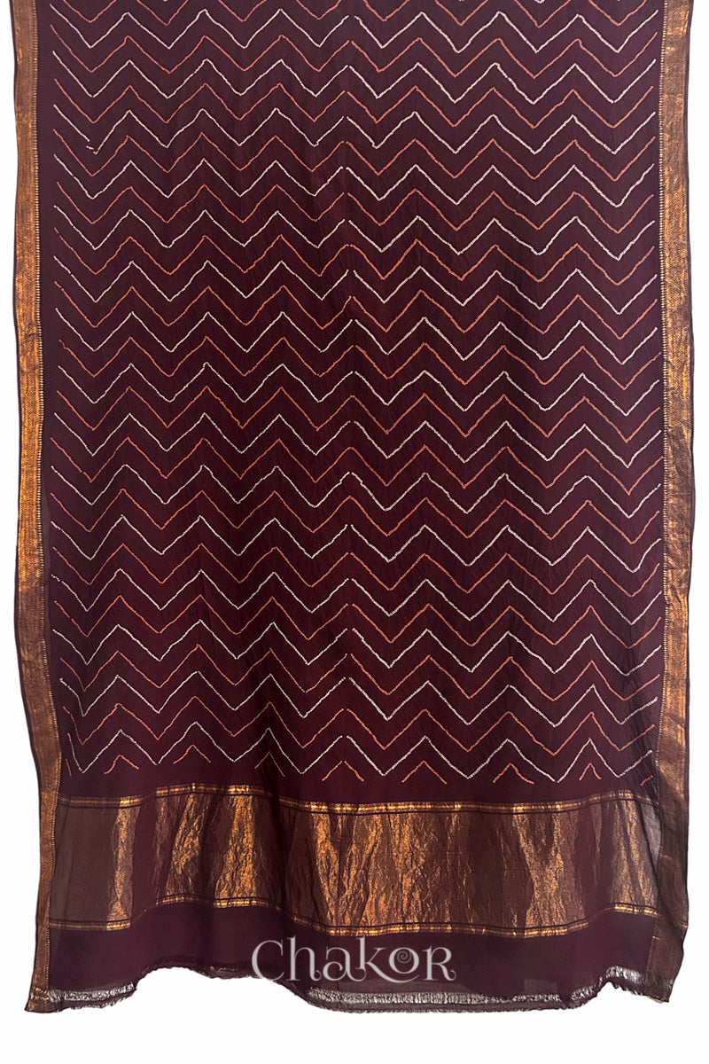 Maroon saree, flat draped with Rai Bandhej zigzag pattern against white background and 'Chakor' brand watermark.

