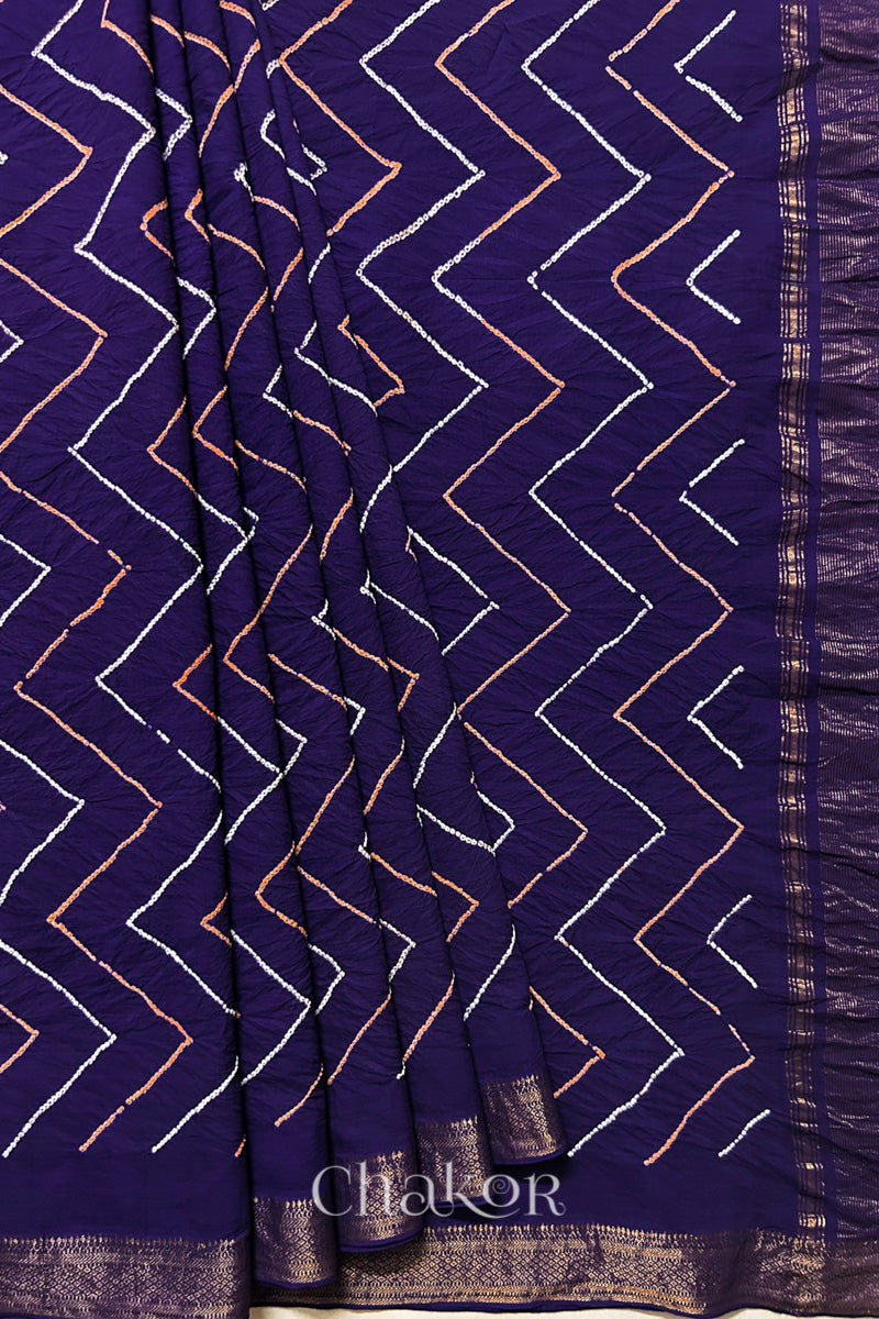 Purple saree, neatly arranged in pleats with Rai Bandhej zigzag pattern and 'Chakor' brand watermark.

