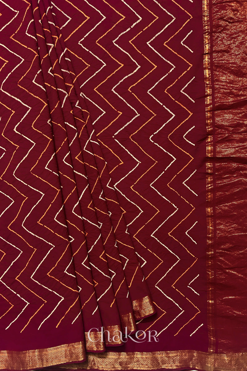 Red saree, neatly arranged in pleats with Rai Bandhej zigzag pattern and 'Chakor' brand watermark.
