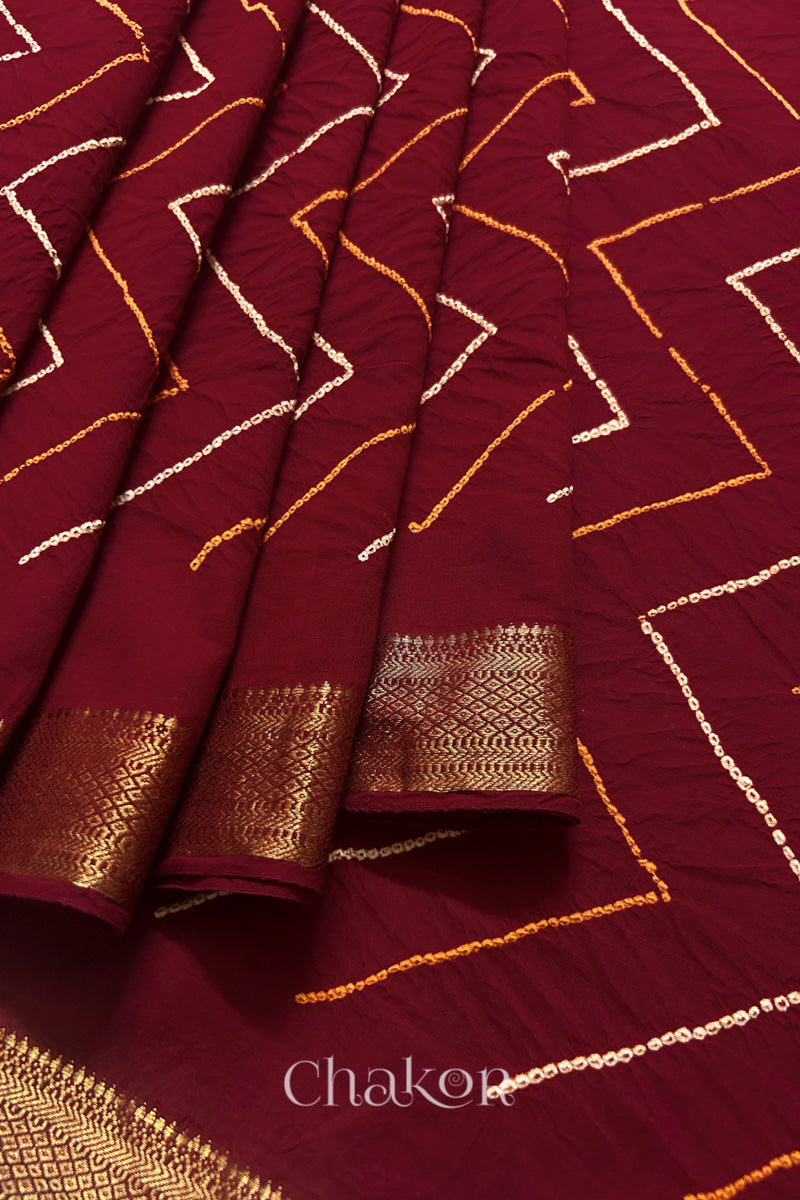 Close-up of Red saree pleats with rai bandhani and zari weaving showcasing beautiful craftsmanship.
