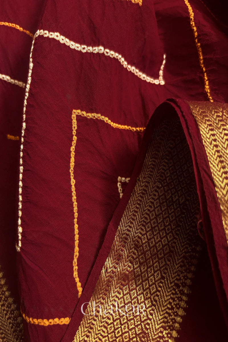 Close-up of Red sarees featuring rai bandhani in zig zag patttern and zari weaving showcasing beautiful craftsmanship.
