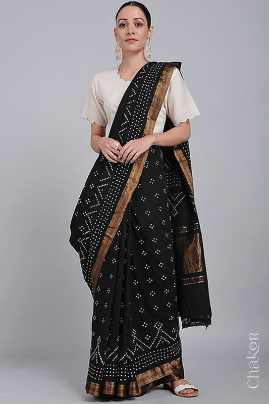 Woman wearing a black saree with white bandhani designs, featuring golden zari borders. 