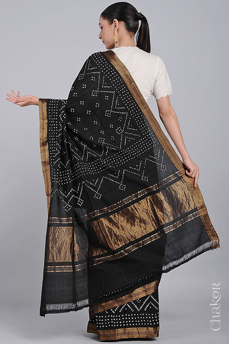 Woman wearing a black saree with white bandhani designs, showcasing golden pallu and zari borders.