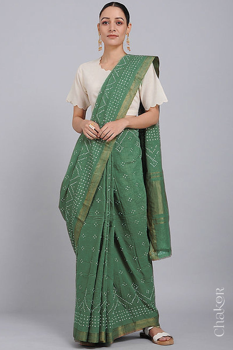 Woman wearing a moss green saree with white bandhani designs, featuring golden zari borders. 