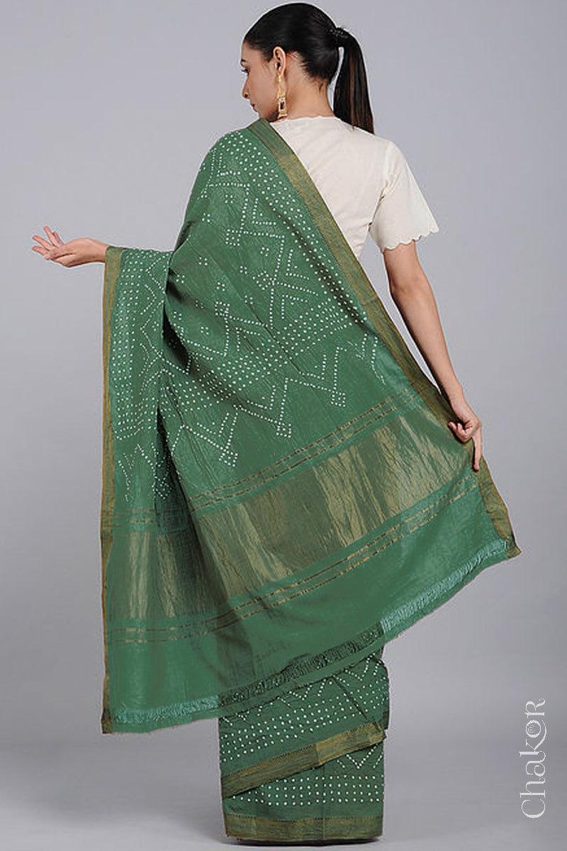 Woman wearing a moss green saree with white bandhani designs, showcasing golden pallu and zari borders.