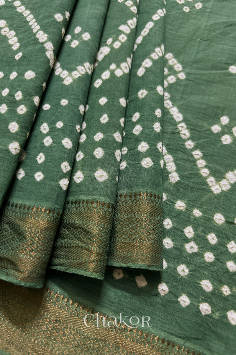 Close-up of moss green saree, arranged in pleats with rai bandhani and golden border showcasing beautiful craftsmanship.
