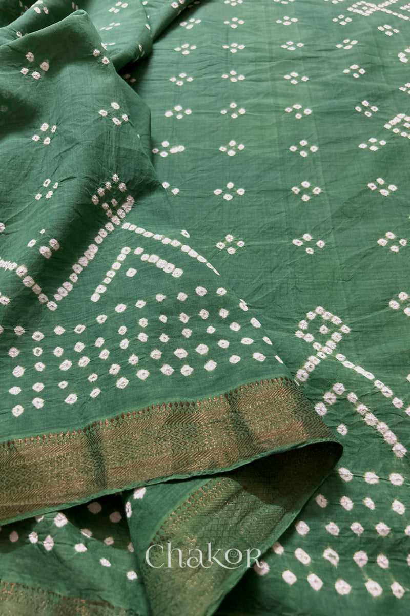 Close-up of moss green saree, folded golden zari border & rai bandhani showcasing beautiful craftsmanship.
