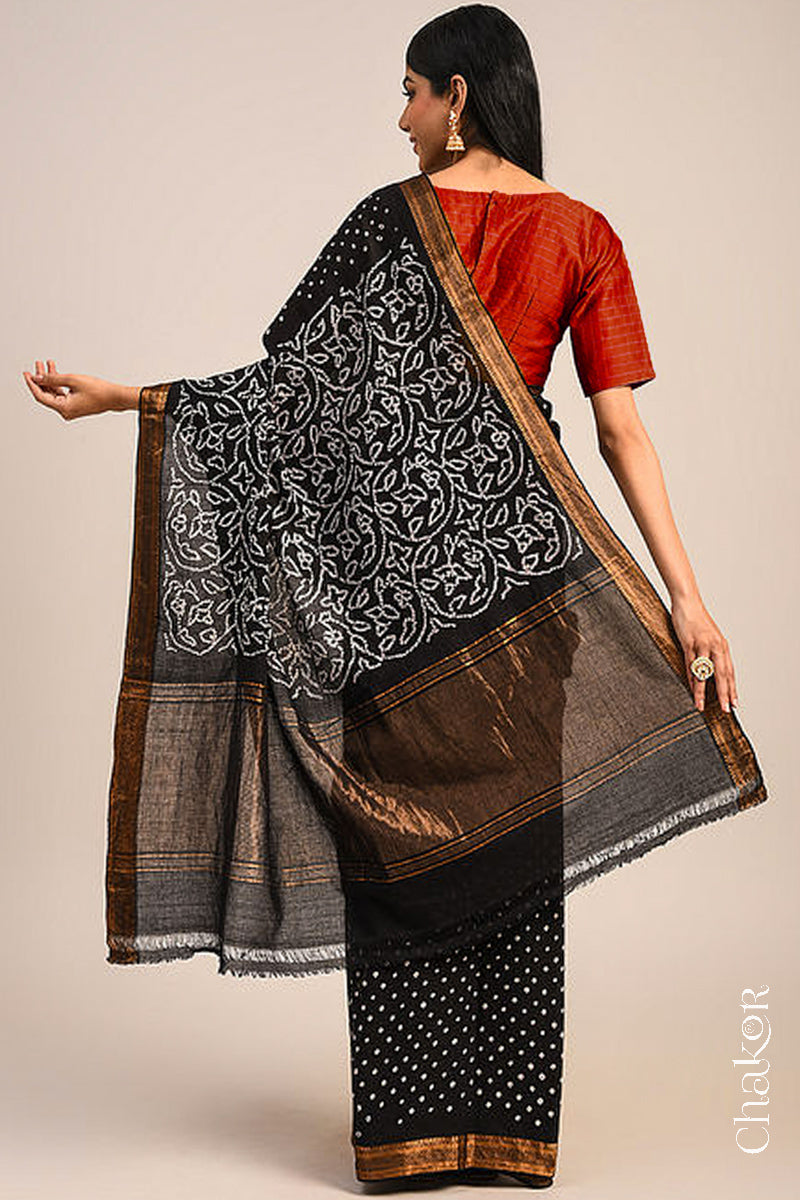 Woman wearing a black bandhani saree showcasing intricate tie dye design on pallu and zari border.