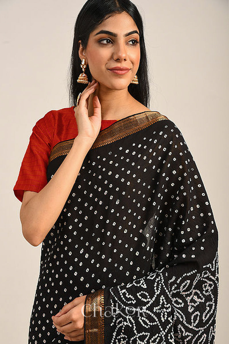 Woman wearing a black bandhej saree with white bandhani dots and golden border.